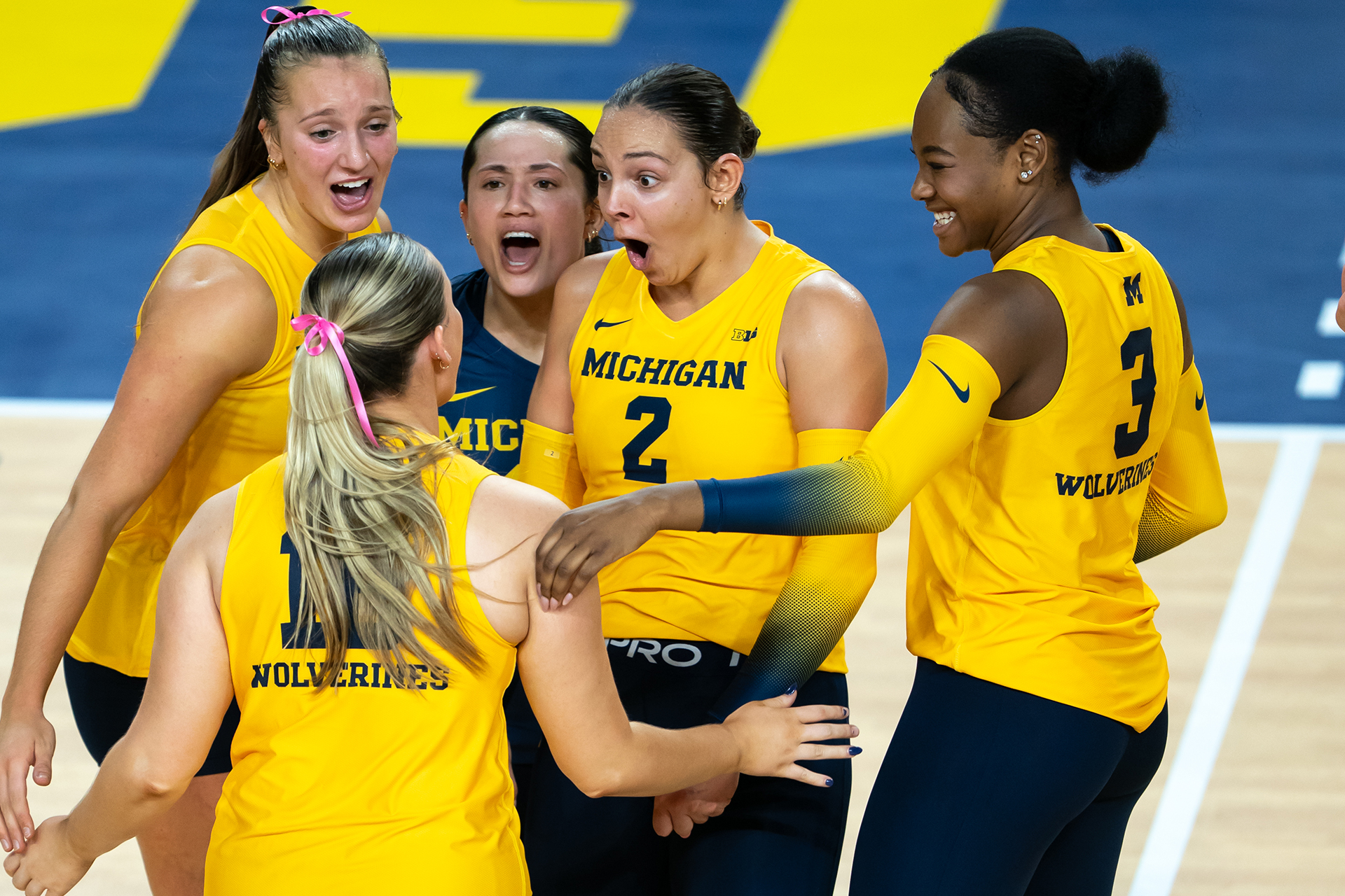 Michigan volleyball players cheering in a huddle and wearing maize jerseys