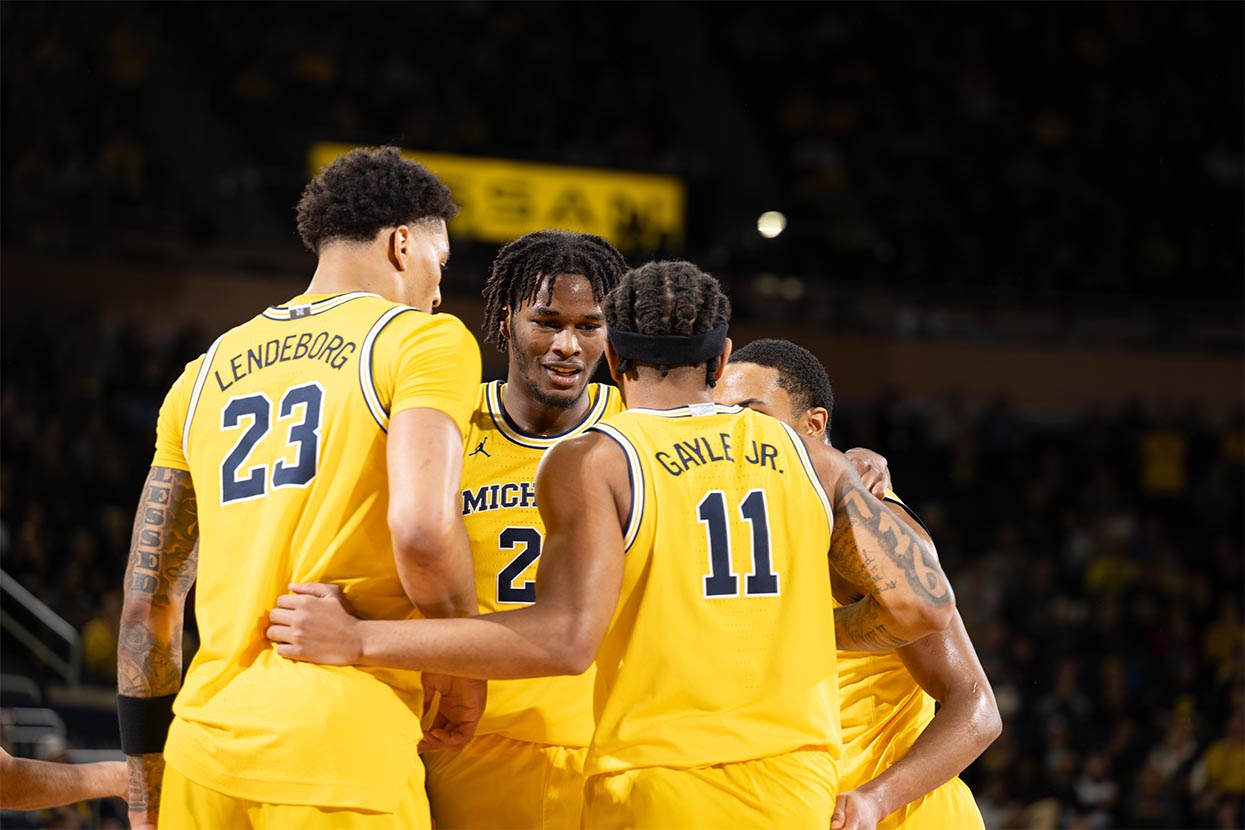 Men's basketball team huddle. Players are wearing maize uniforms