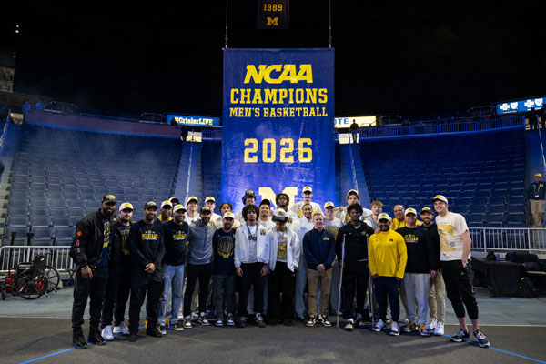 Men's basektball team in Crisler in front of the 2026 NCAA Champions banner